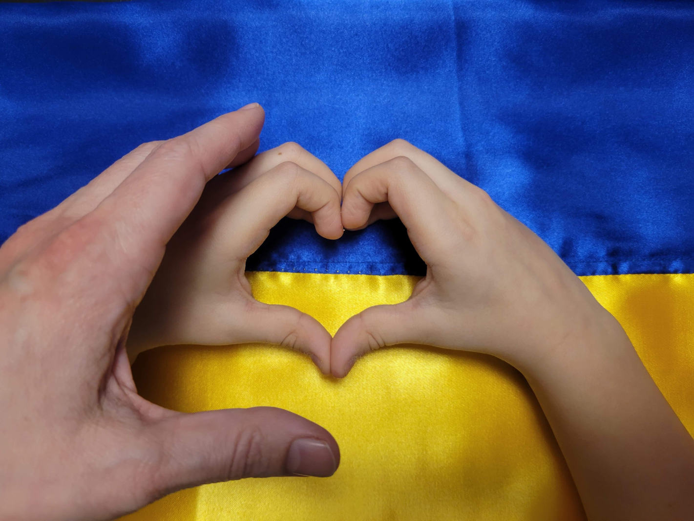hands curled into hearts over Ukrainian flag
